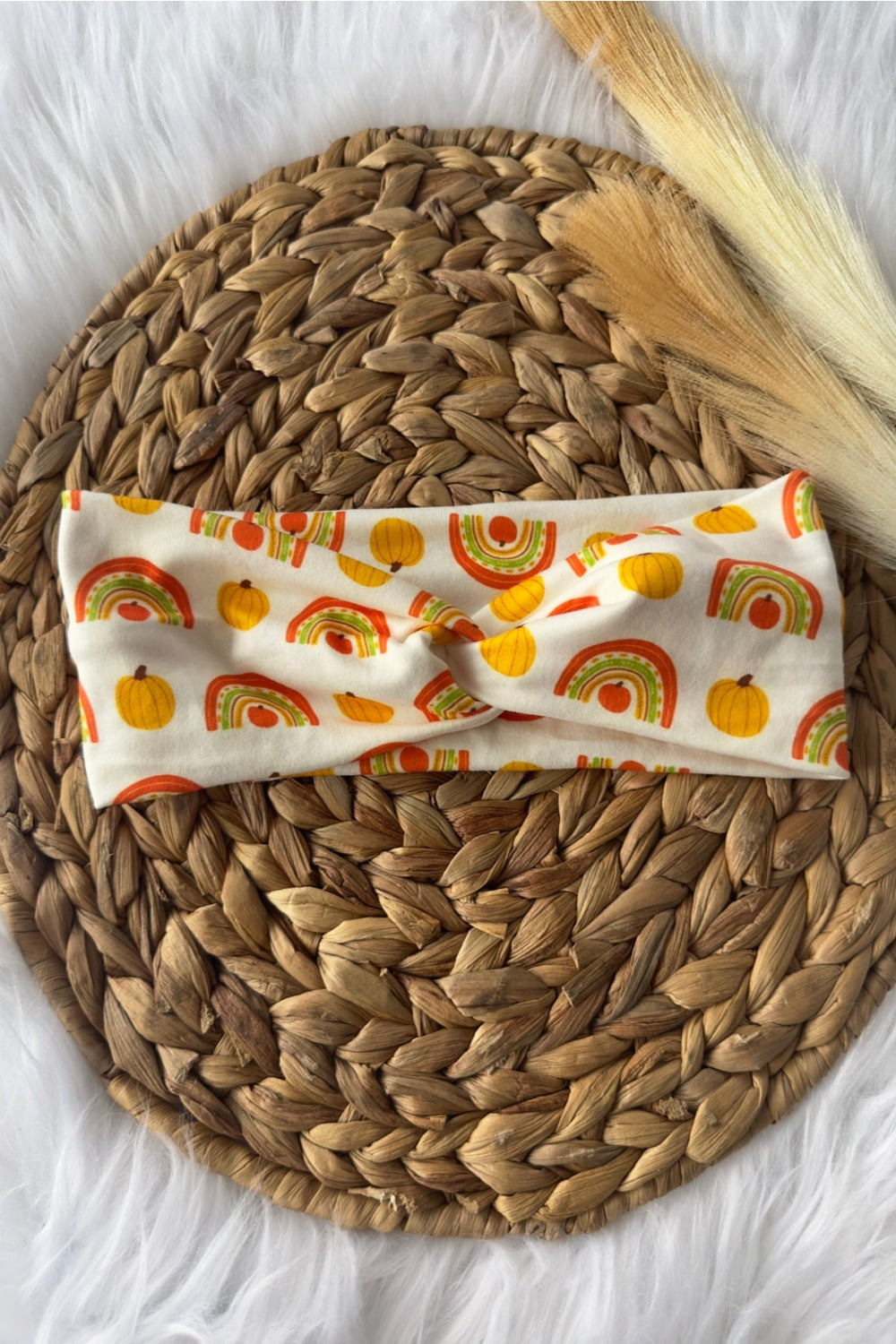 Boho stye fall colored rainbows and pumpkins on a white twist headband. Placed on a wicker photo prop.