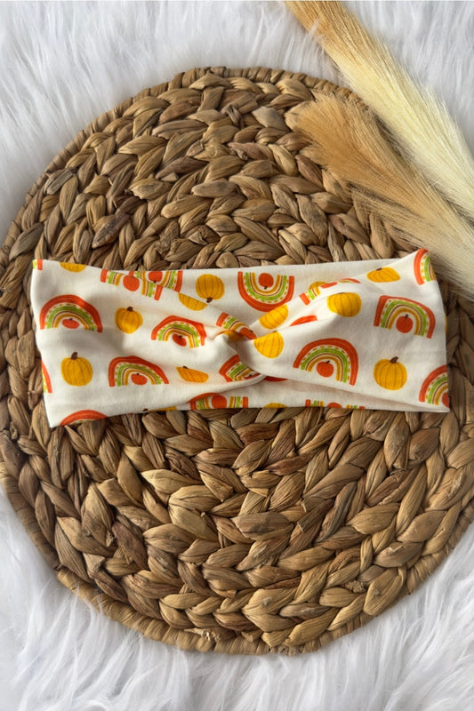 Boho stye fall colored rainbows and pumpkins on a white twist headband. Placed on a wicker photo prop.